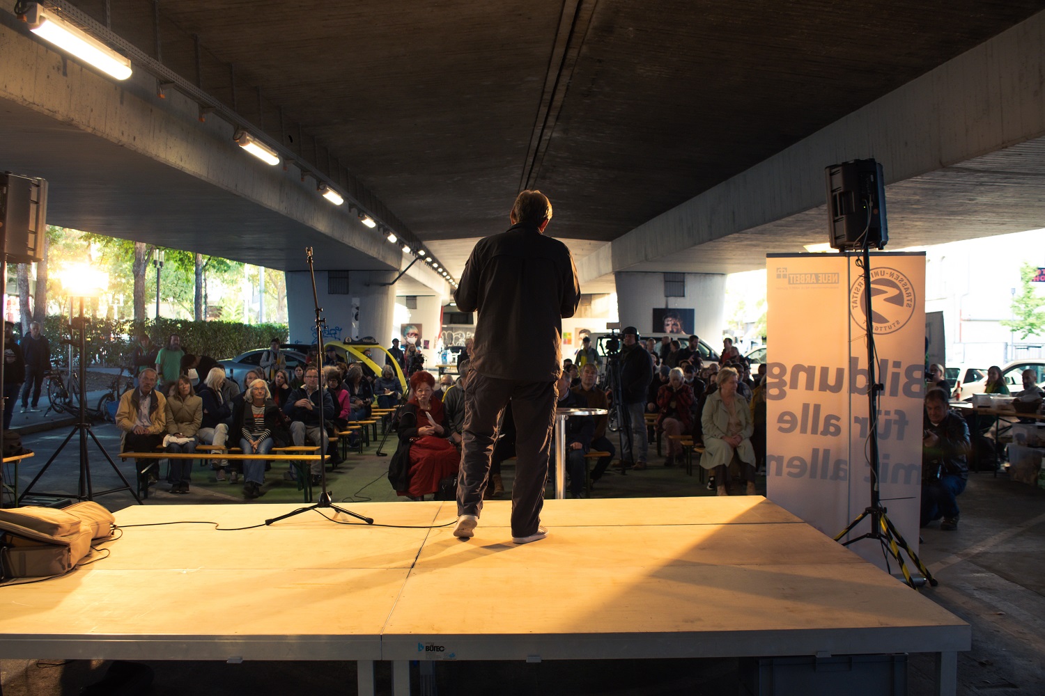 Ein Mann steht vor einem Publikum auf einer Bühne im Straßenraum