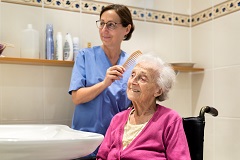 Pflegekraft kämmt alte Frau im Bad